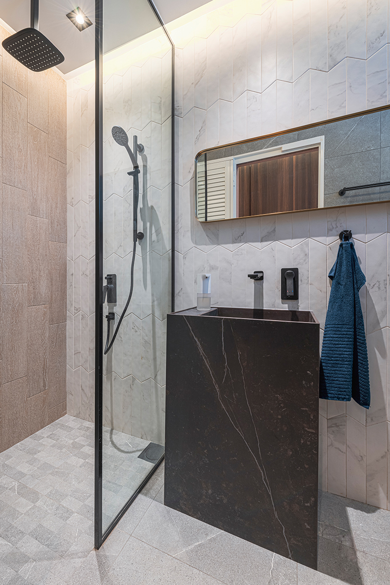 Herringbone-laid marble tiles and matte black fixtures give this bathroom display a refined, hotel-like finish.
