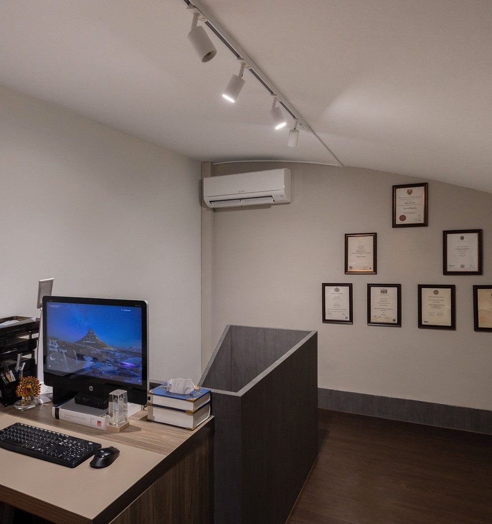 A built-in desk faces a wall of framed certificates and a curved partition, giving the home office a considered, professional corner of its own.