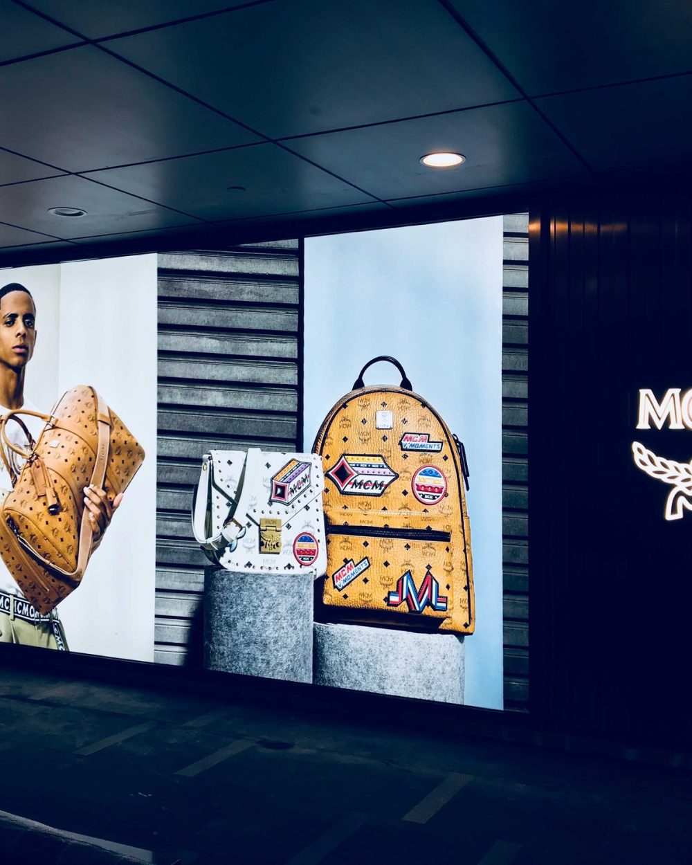 An illuminated MCM campaign wall and logo signage lit up after the mall has closed.