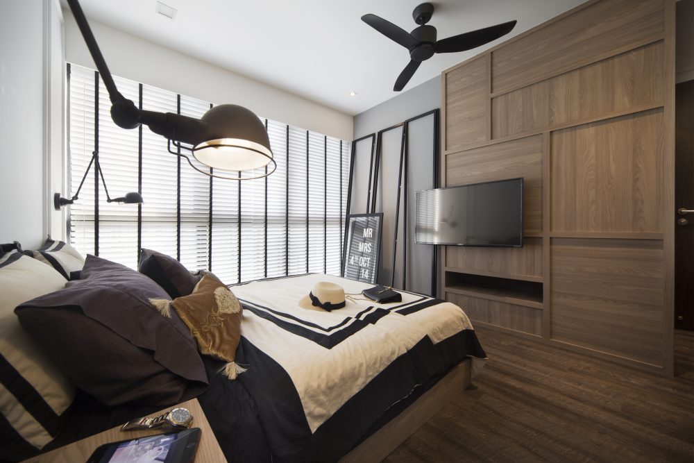 An oversized articulating lamp and steel-framed room divider bring an industrial edge to the bedroom, beside a timber TV feature wall.