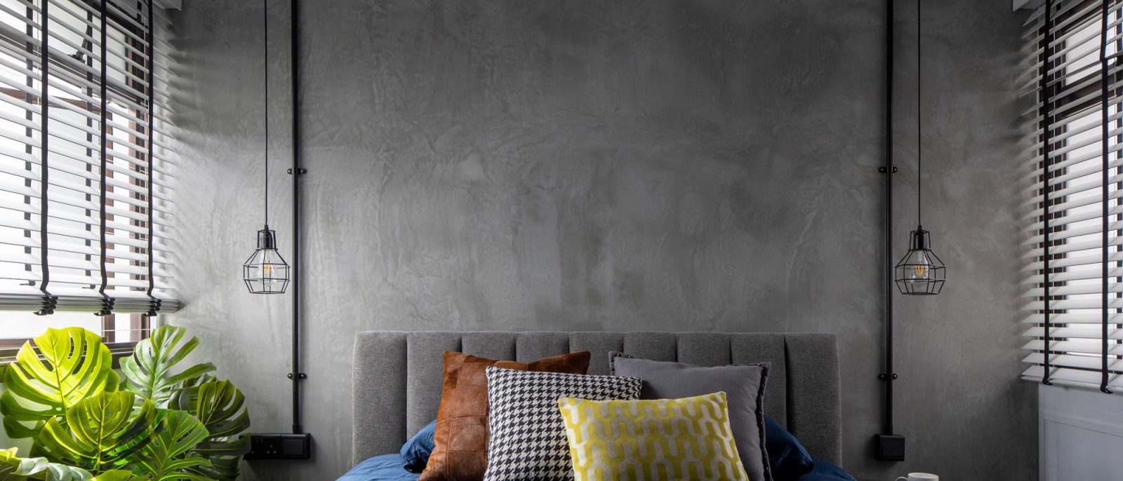 Raw concrete plaster wraps the headboard wall, flanked by exposed black conduit pipes ending in cage pendant lights.