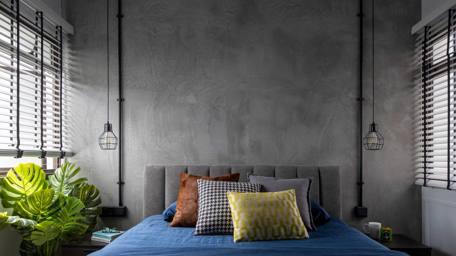 Raw concrete plaster wraps the headboard wall, flanked by exposed black conduit pipes ending in cage pendant lights.