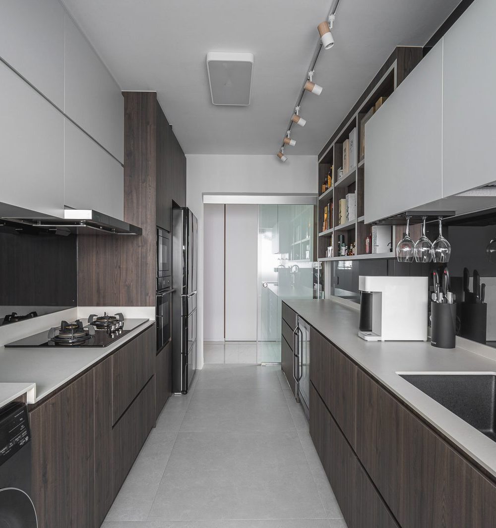 Wine glasses hang beneath the upper cabinets, with open shelving for spirits and cookbooks lit warmly above the black splashback.