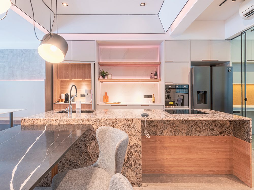 A granite-topped island and backlit marble display shelf, warmed by soft pink accent lighting, showcase one of the studio's kitchen concepts.