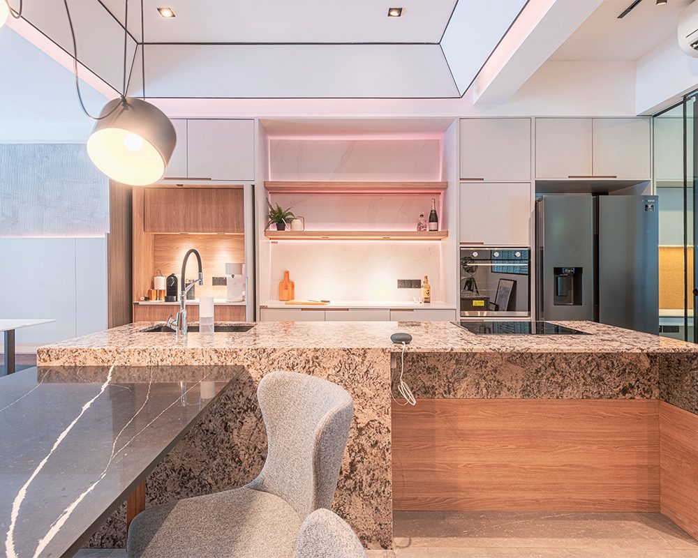 A granite-topped island and backlit marble display shelf, warmed by soft pink accent lighting, showcase one of the studio's kitchen concepts.