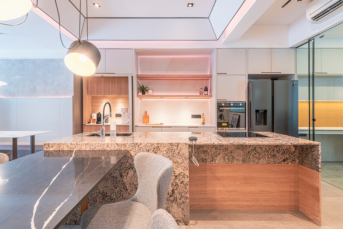 A granite-topped island and backlit marble display shelf, warmed by soft pink accent lighting, showcase one of the studio's kitchen concepts.
