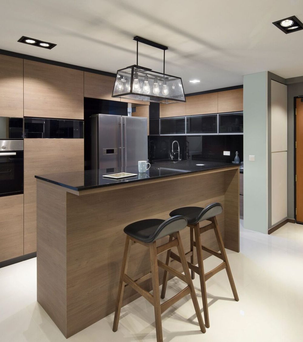 A boxy black pendant hangs over the kitchen island, framed by warm timber cabinetry and a glossy black upper unit run leading to the front door.