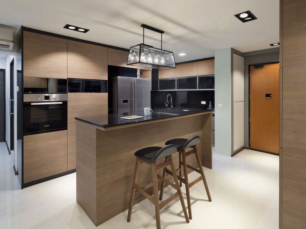 A boxy black pendant hangs over the kitchen island, framed by warm timber cabinetry and a glossy black upper unit run leading to the front door.