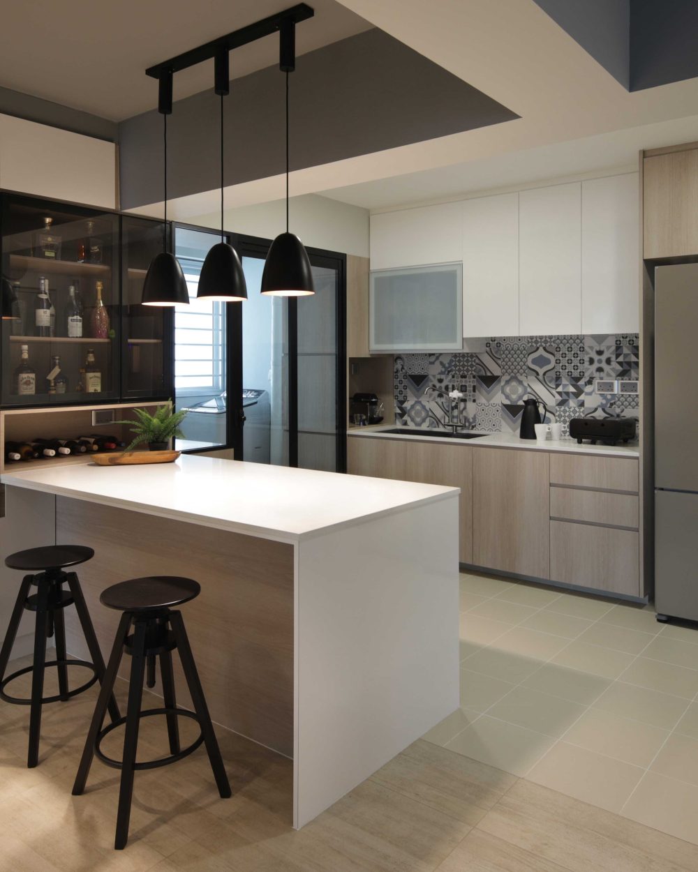 A cluster of black pendant lights hangs over a white-topped kitchen island, with a glass-fronted bar cabinet for wine and spirits built in above.