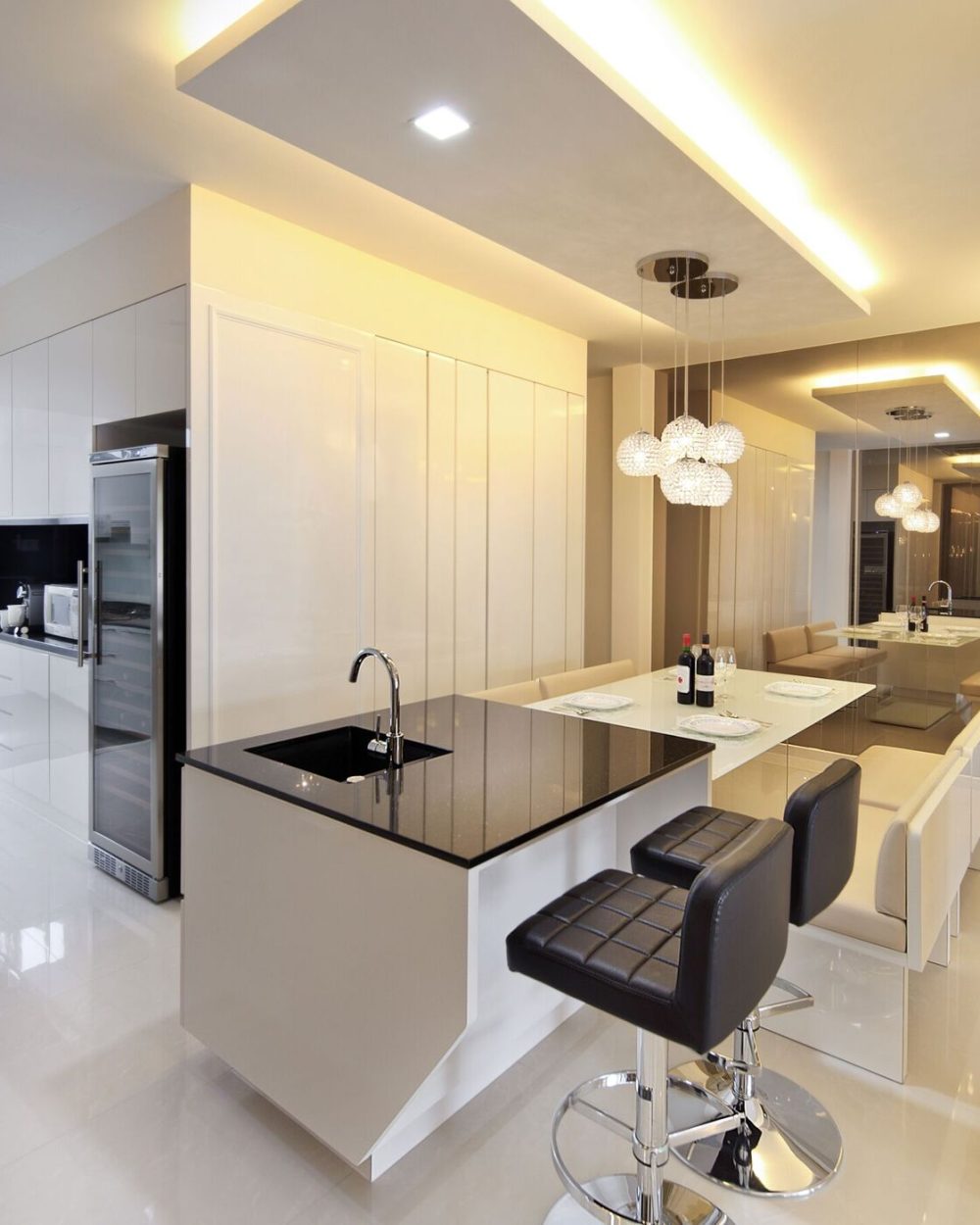 A white gloss island with a black stone counter includes built-in wine storage, lit by the same crystal pendant cluster.