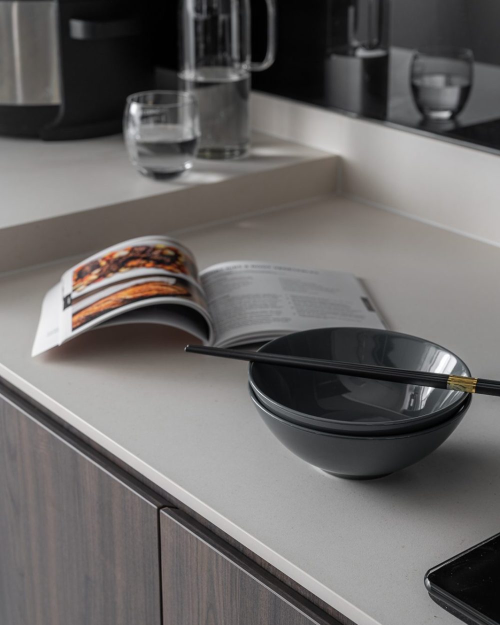 A cookbook stays open on the counter beside a stack of bowls and chopsticks, ready for the next meal.
