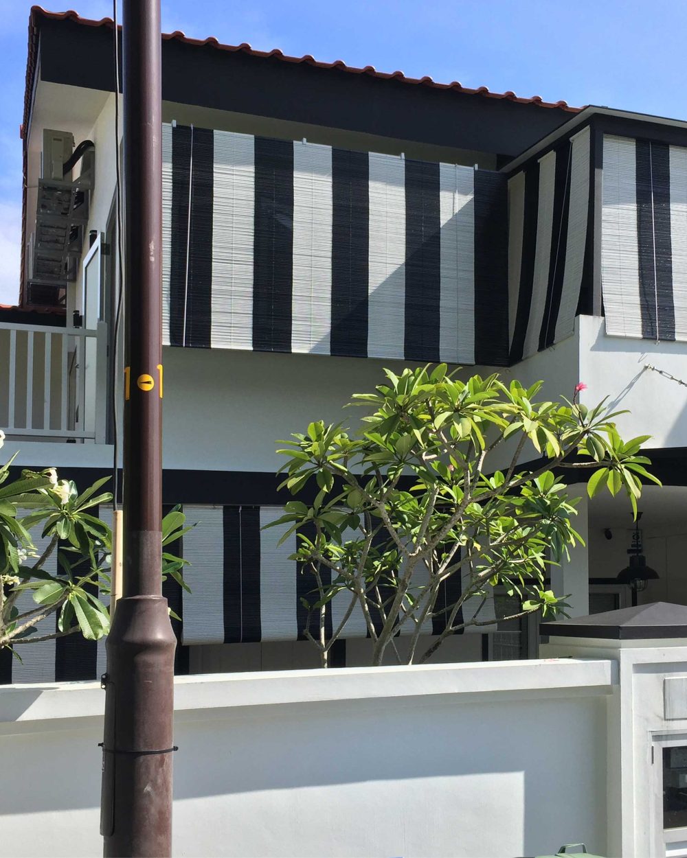 An open-air balcony with slatted railings sits above the entrance, framed by lush tropical planting that softens the home's crisp monochrome lines.