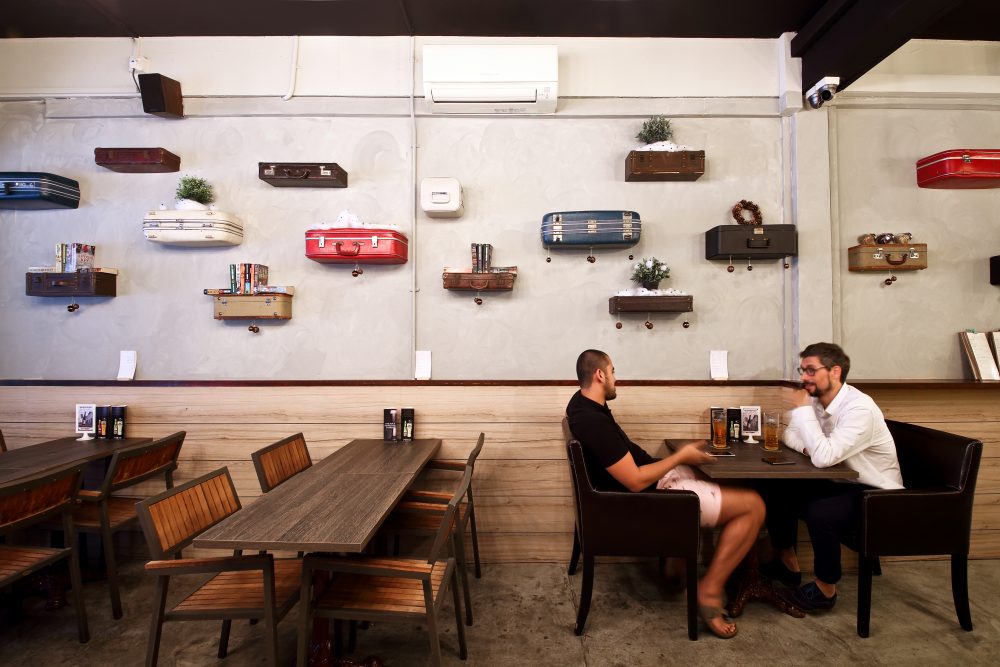 The suitcase wall continues above a row of dining tables, giving the bar's main seating area its distinctive character.