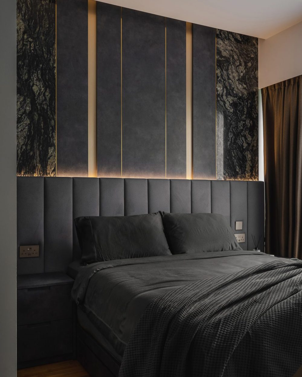 The full headboard wall pairs green-veined marble with brass trim and deep grey channel upholstery for a hotel-suite feel.