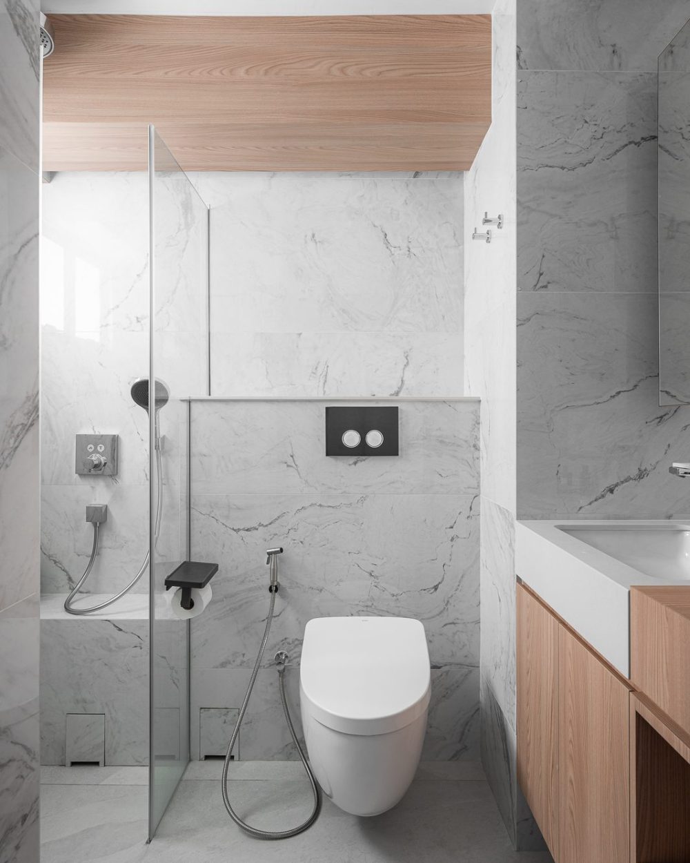 Full-height marble tiling wraps the ensuite bathroom, with a walk-in rain shower and a wall-hung toilet with concealed cistern controls.