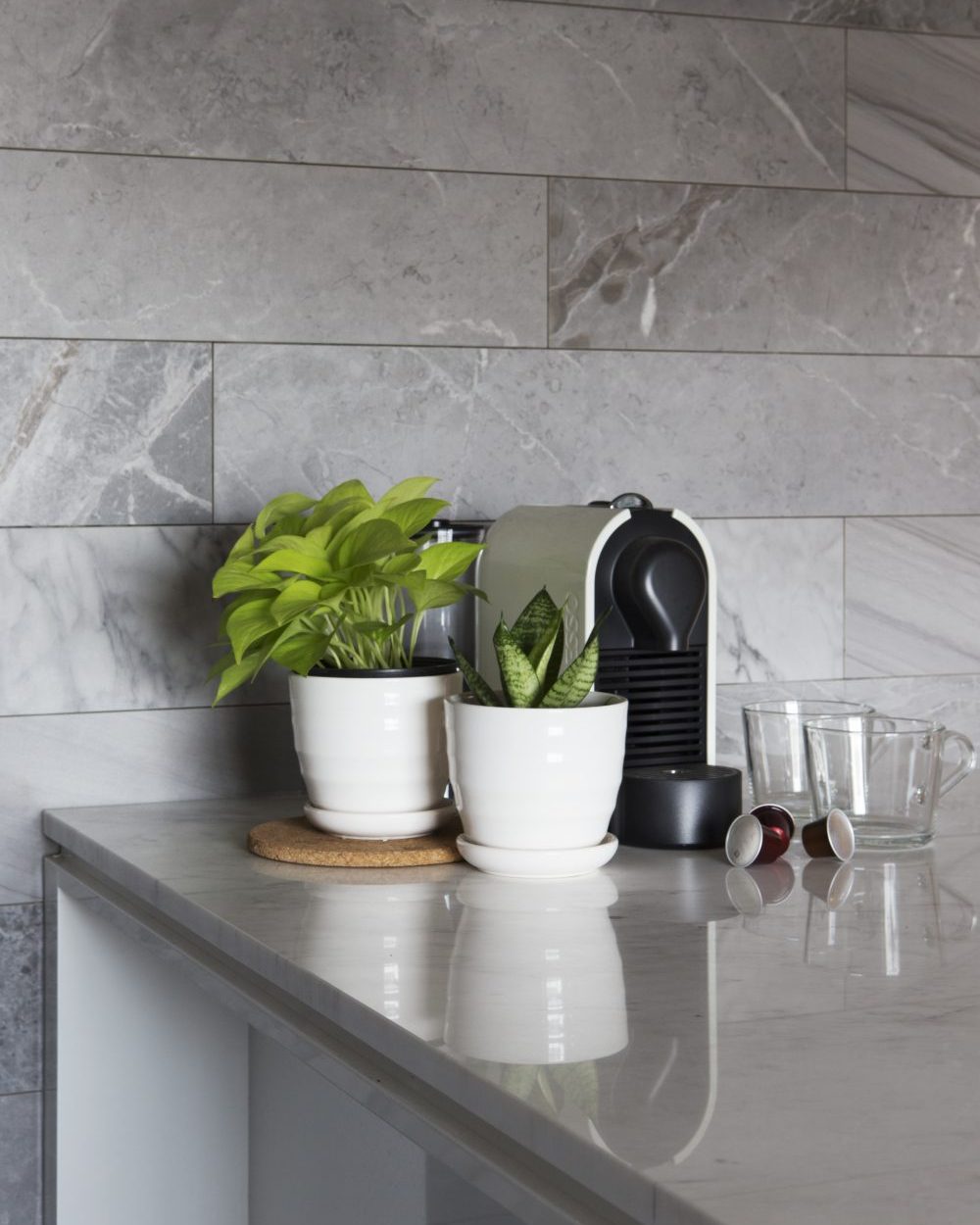 Potted plants and a Nespresso machine sit on the honed marble counter, softening the dining area's stone surfaces.