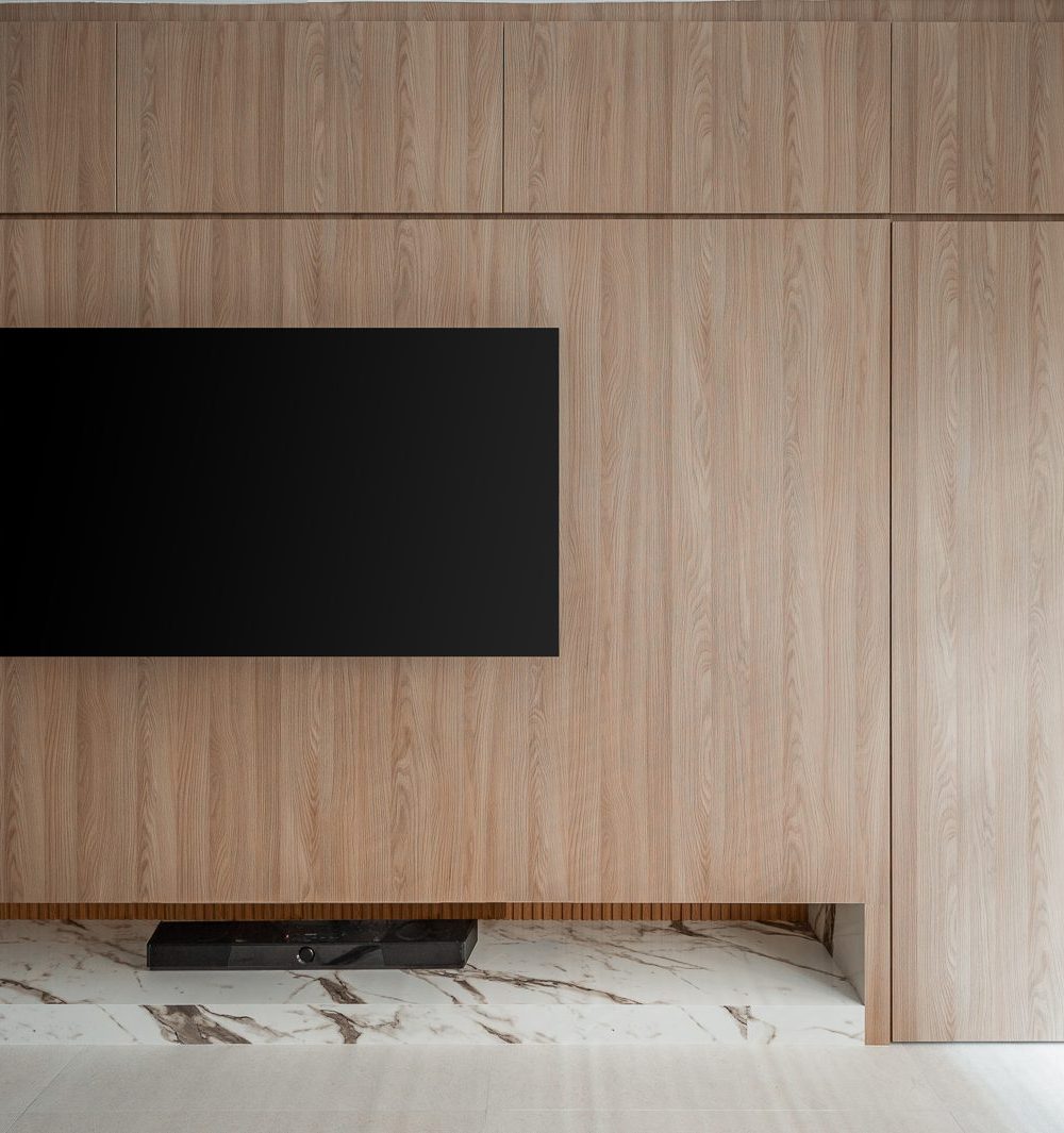 A recessed marble ledge with warm LED lighting sits beneath the wall-mounted TV, framed by the timber panelling's clean vertical lines.