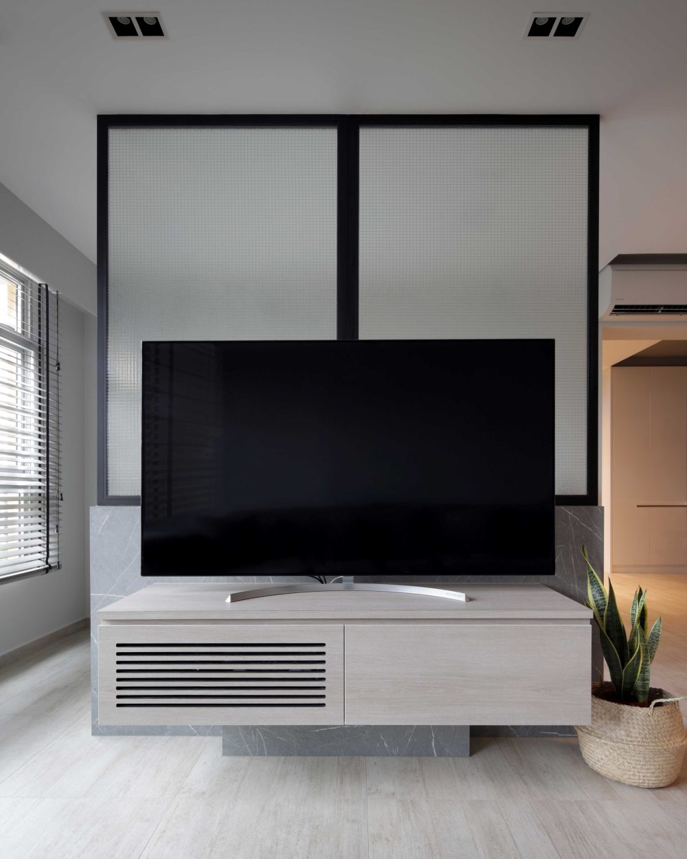 A frosted glass screen rises behind the TV console, set on a marble-clad plinth that grounds the living room's feature wall.
