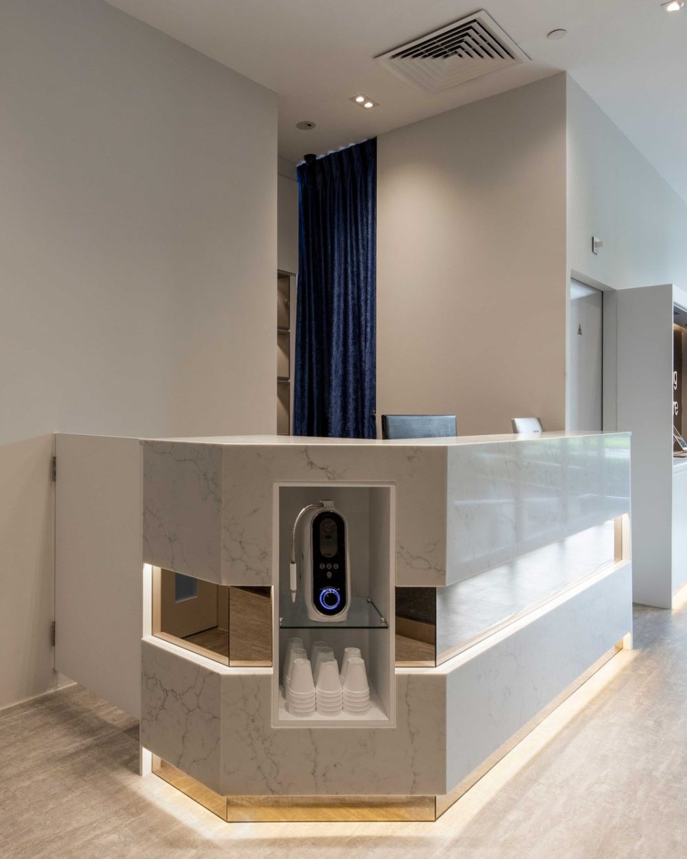 A waterfall-edge marble reception counter greets patients, with a deep blue curtain and backlit display niche adding a touch of warmth.