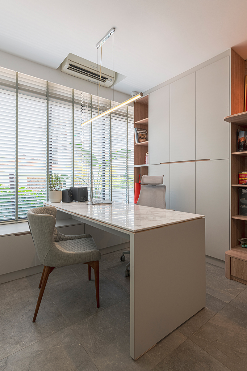 A marble-topped desk and built-in wood-and-white cabinetry demonstrate a home office concept, lit by a slim pendant light.