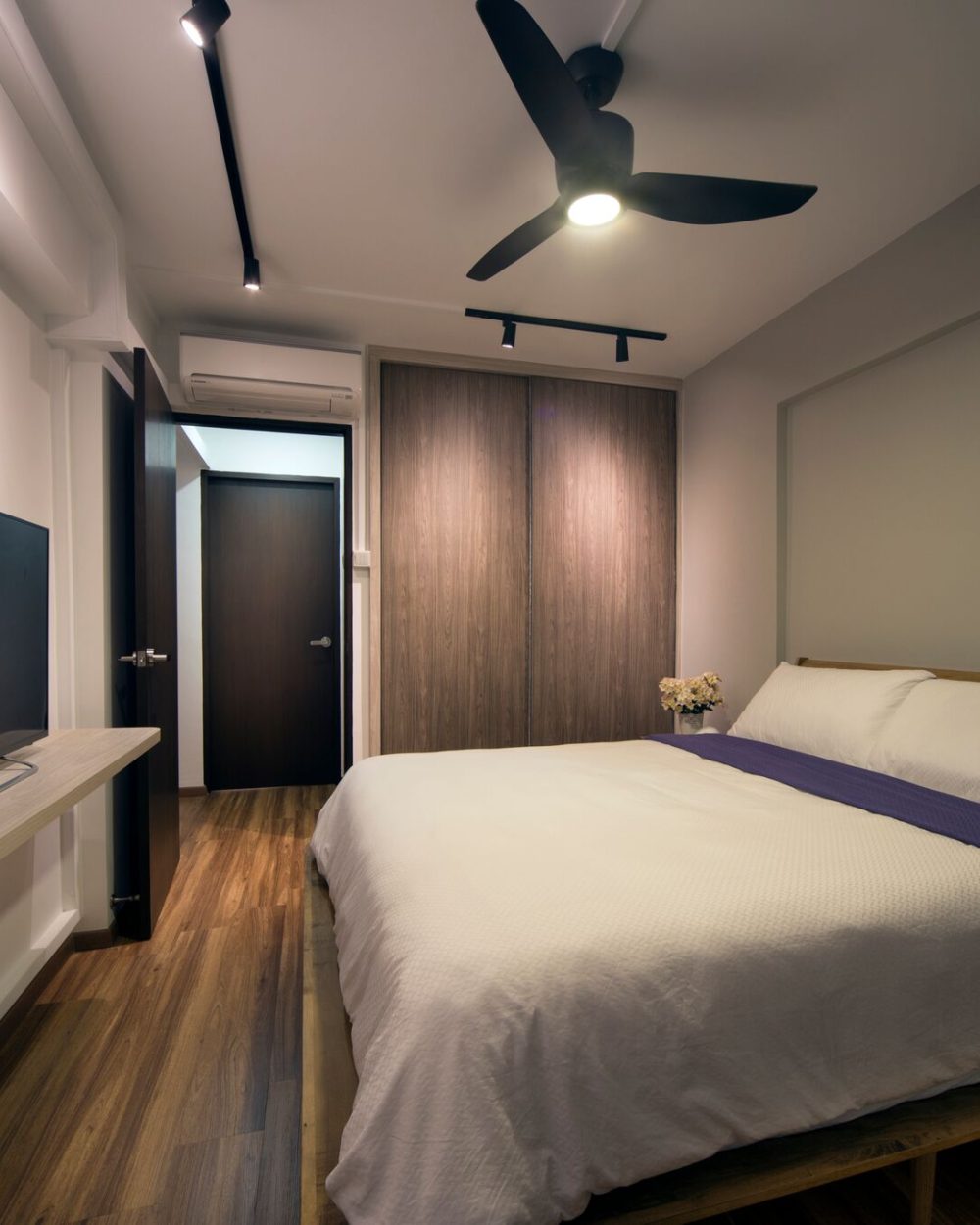 Timber-toned sliding wardrobe doors and a floating TV console flank the bed, set against an upholstered headboard wall.