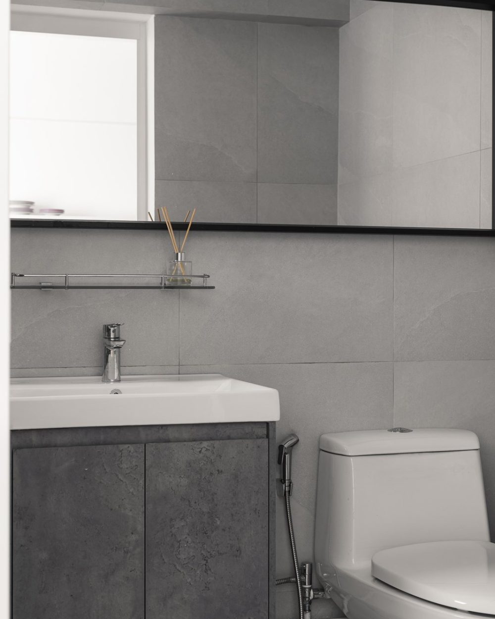 Minimalist grey bathroom with concrete-finish vanity cabinet, white basin, black-framed mirror and one-piece toilet