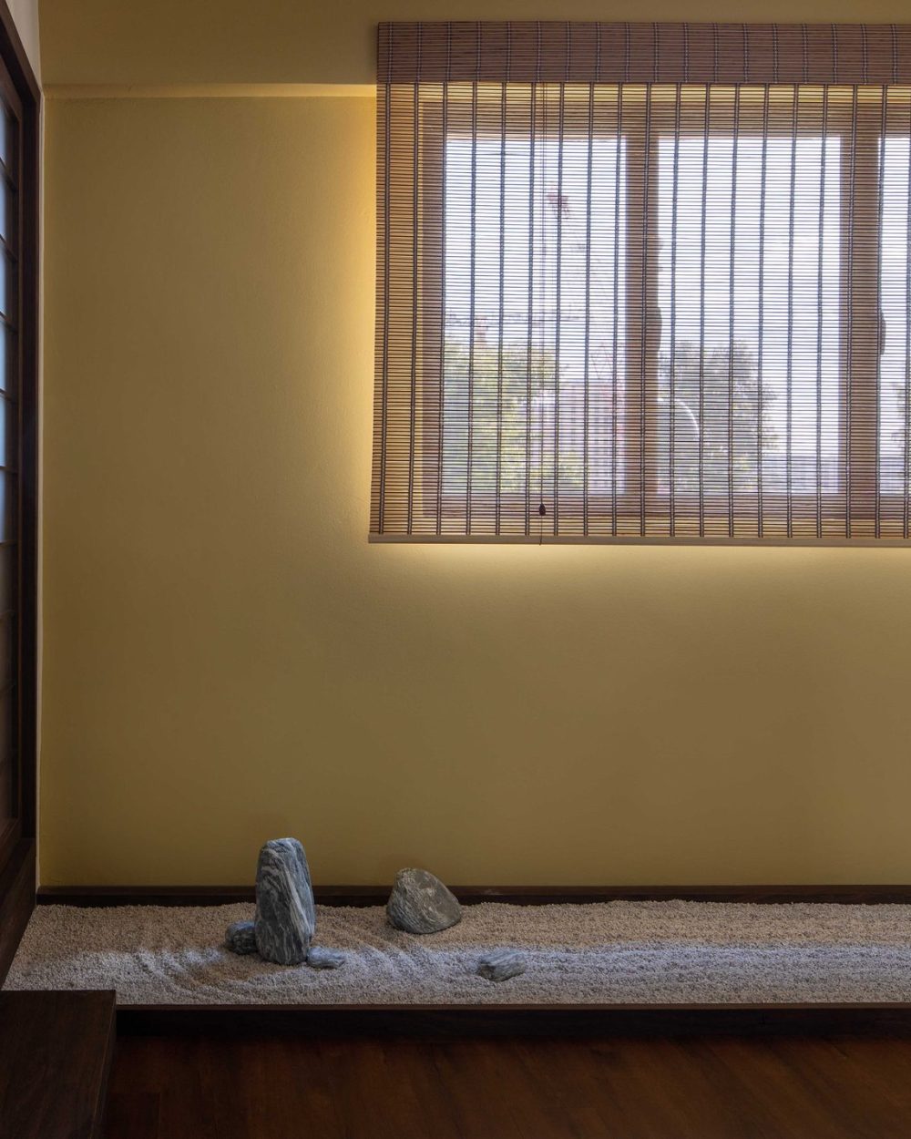 A single upright stone stands in raked gravel against a warm mustard wall, beside the tea room's shoji screen.