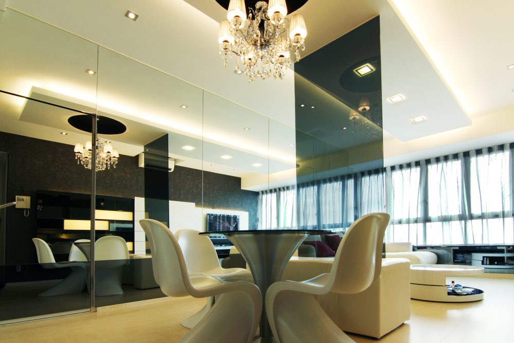 A full-height mirror wall and crystal chandelier open up the dining space, paired with a round table, sculptural white dining chairs and a glossy blac