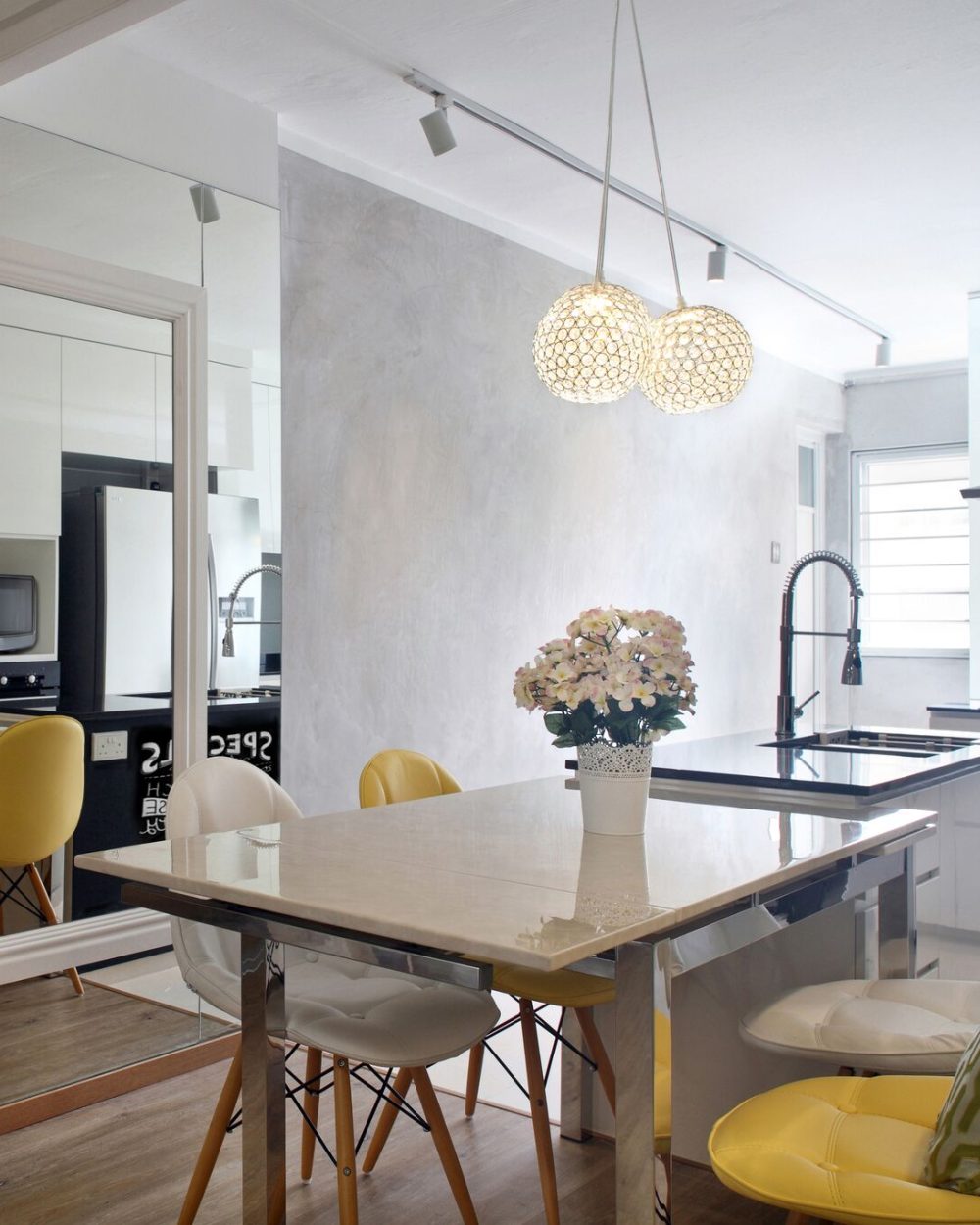 Crystal ball pendants hang over a marble-topped dining table, with a full-height mirror wall visually doubling the open kitchen beyond.