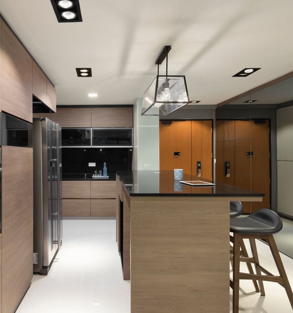 Mirrored cabinet fronts extend the kitchen's sense of depth, reflecting the timber-toned island and pendant light back down the hallway.