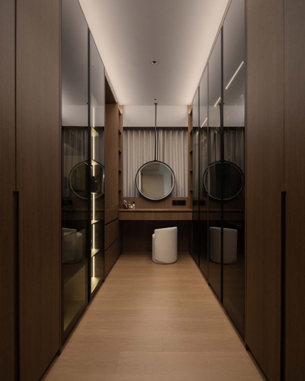 A run of mirrored wardrobe doors lines both sides of the walk-in corridor, doubling the sense of space as it leads to a dedicated dressing area.