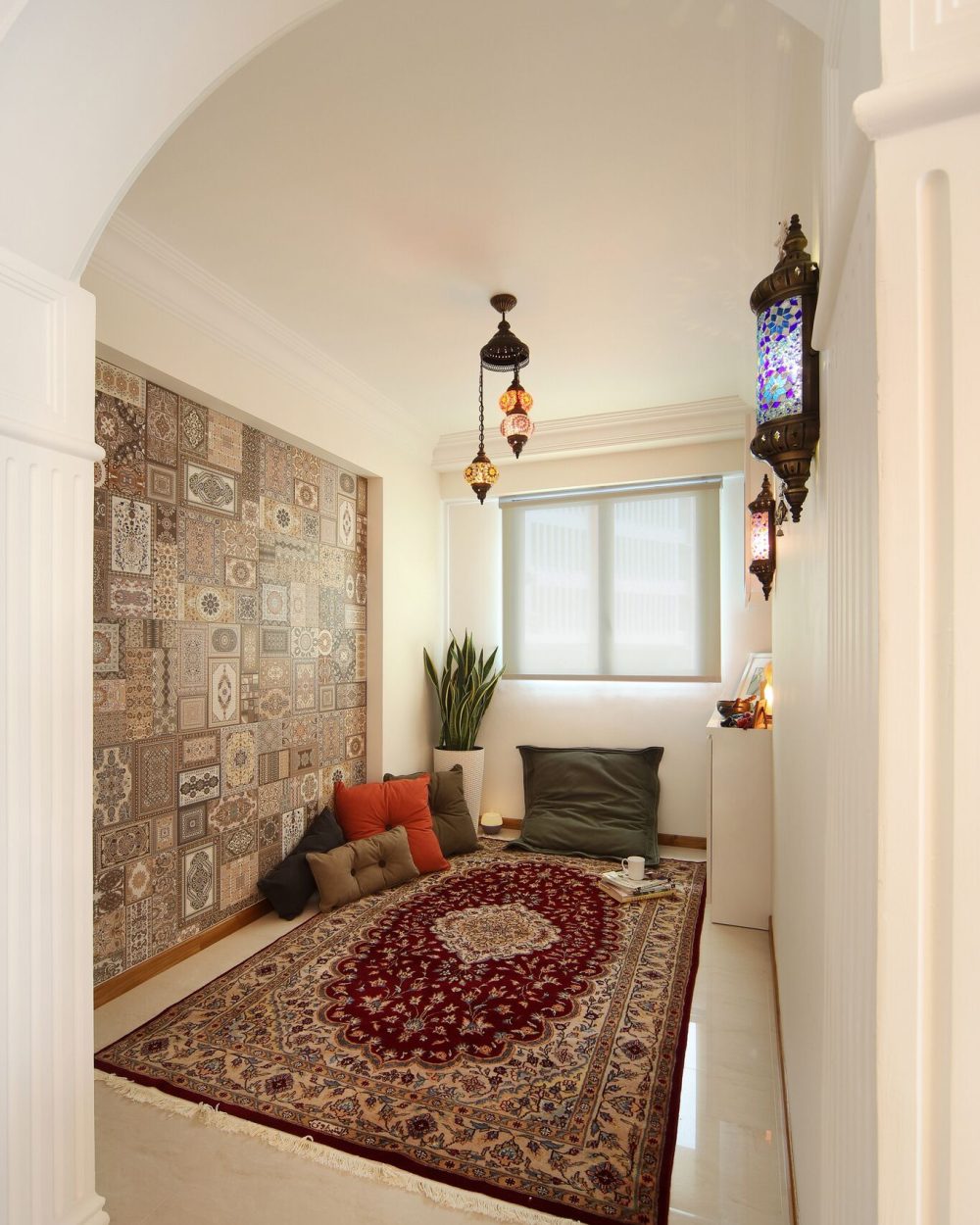 A patchwork tile feature wall and hanging mosaic lanterns give this quiet corner a Moroccan character, finished with a patterned rug and floor cushion