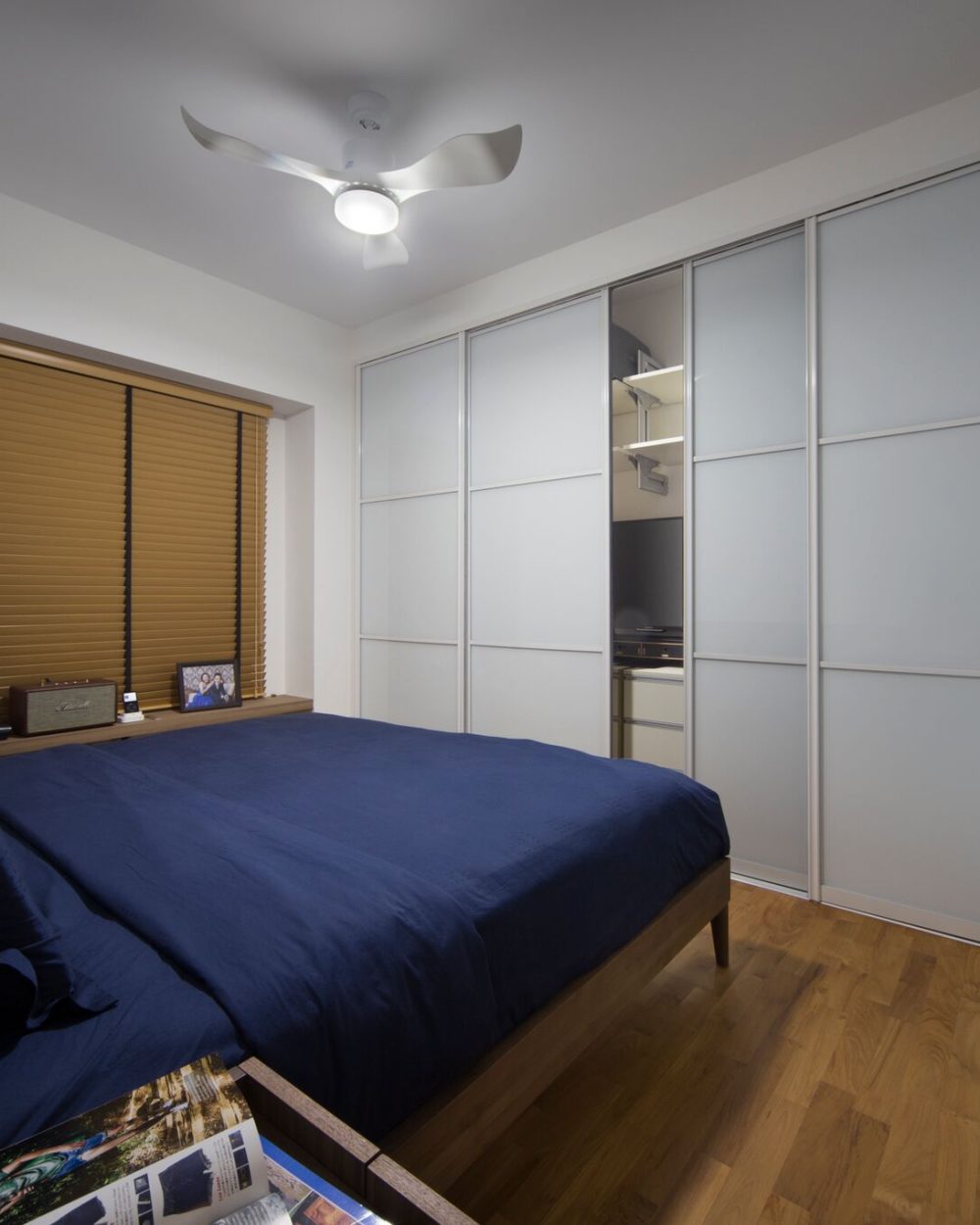 Mustard-toned blinds and a navy bedspread bring warmth to the master bedroom, set against full-height frosted glass wardrobe doors.