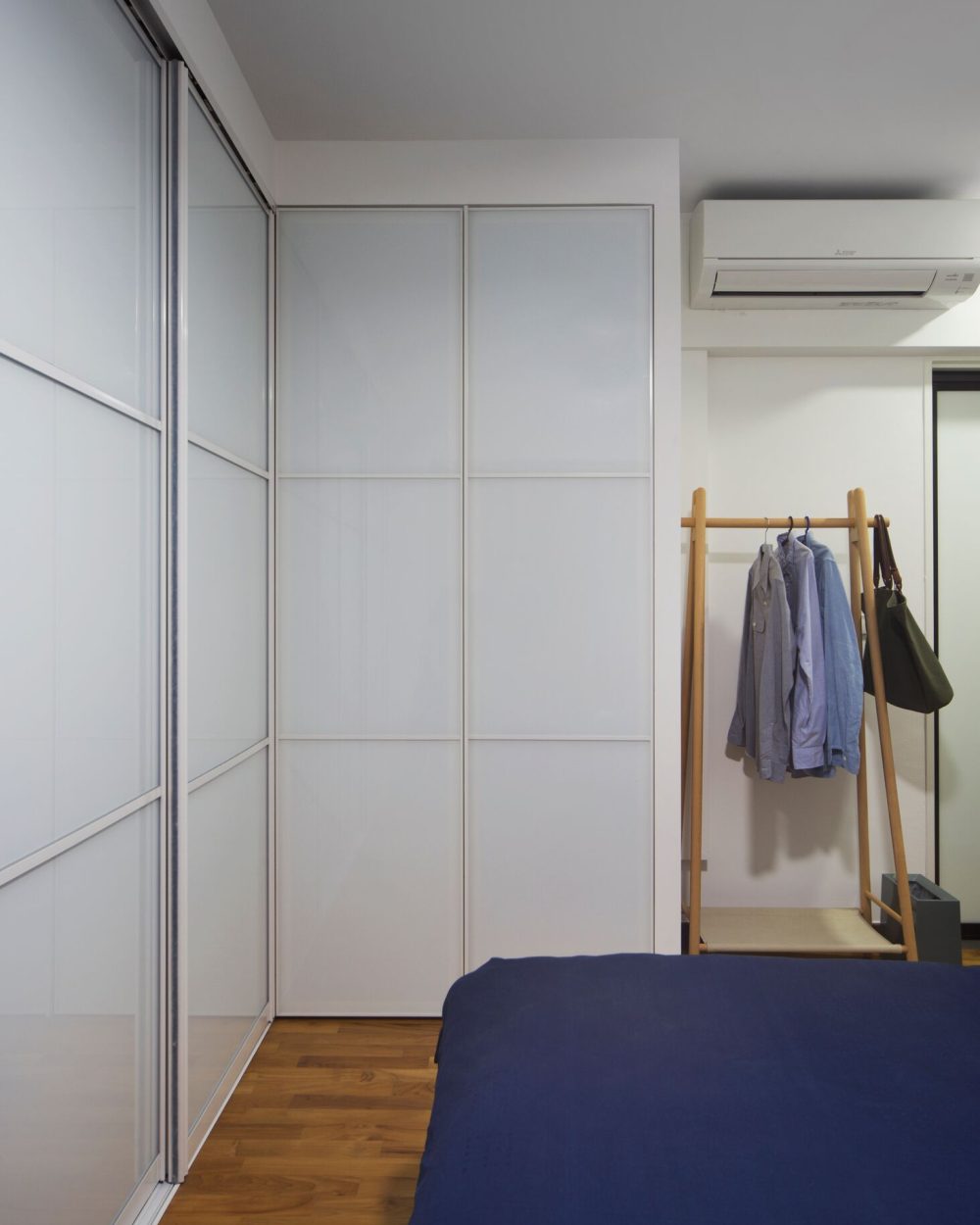 A freestanding timber clothing rack adds flexible, visible storage beside the wardrobe, finished with a woven tote for everyday essentials.