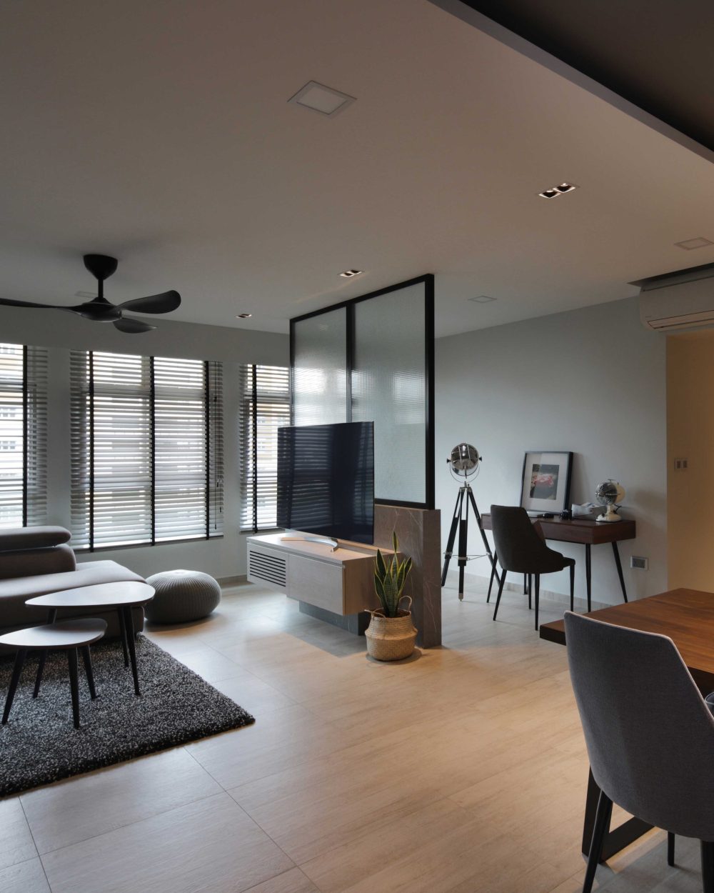 A black-framed glass partition divides the living area from a home office nook, while a statement black pendant hangs low over the dining table.