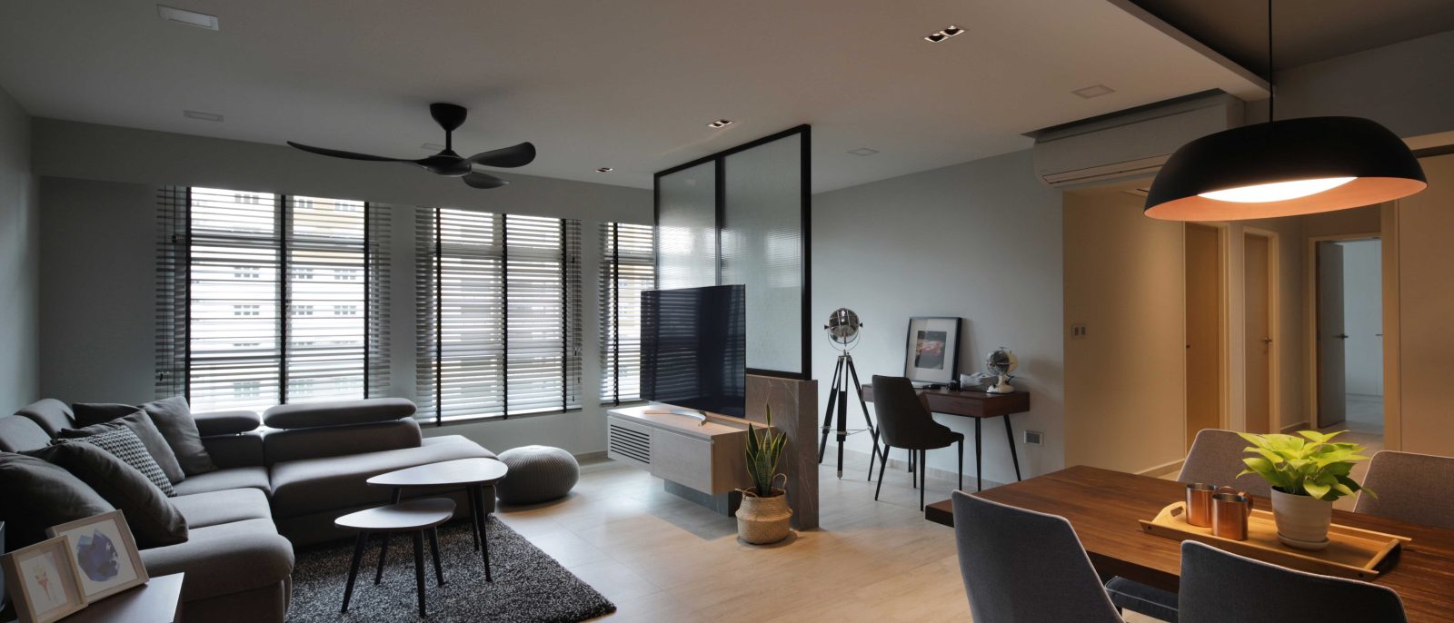 A black-framed glass partition divides the living area from a home office nook, while a statement black pendant hangs low over the dining table.