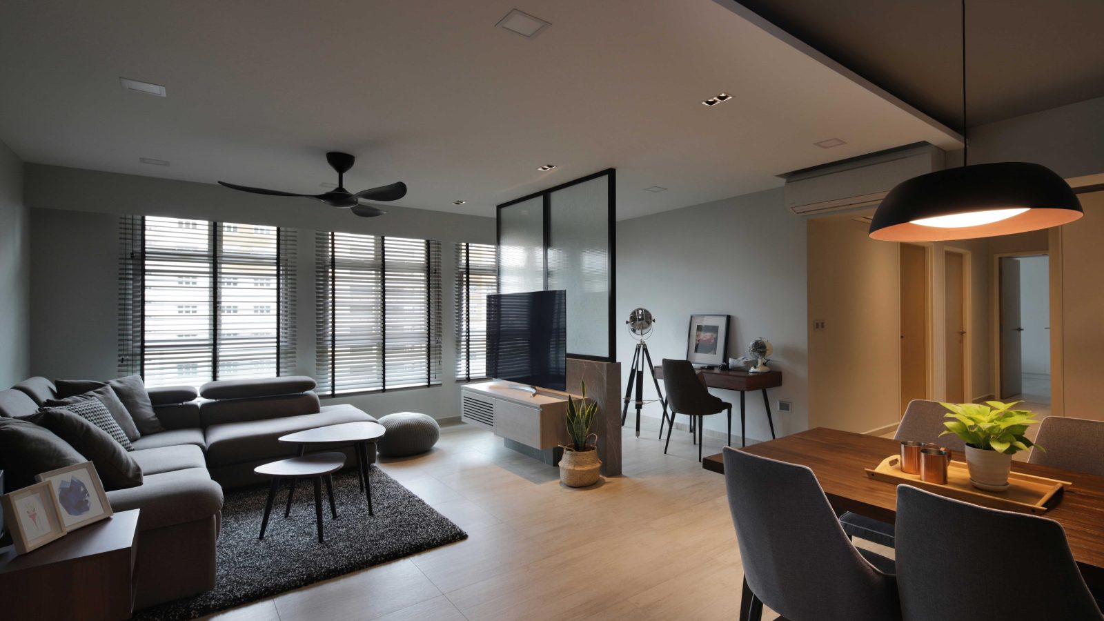 A black-framed glass partition divides the living area from a home office nook, while a statement black pendant hangs low over the dining table.