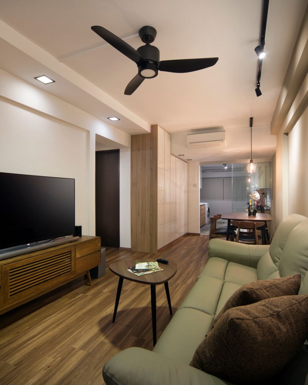 Track lighting and a slim ceiling beam define the living area, with the dining space and utility corridor visible beyond through a run of high-gloss s