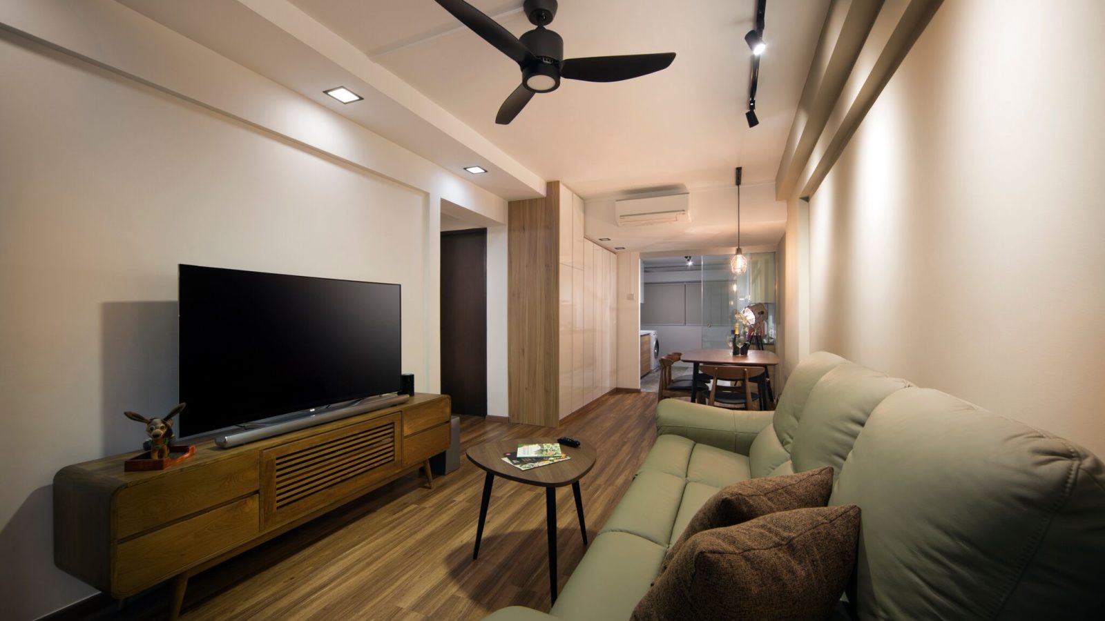 Track lighting and a slim ceiling beam define the living area, with the dining space and utility corridor visible beyond through a run of high-gloss s