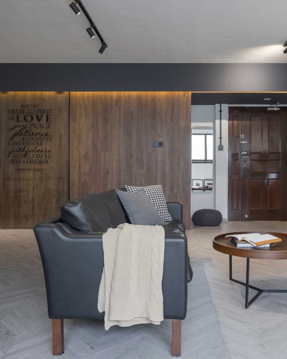 A black leather sofa faces the TV console, with the scripture door, entryway and dining area all visible in one continuous view.