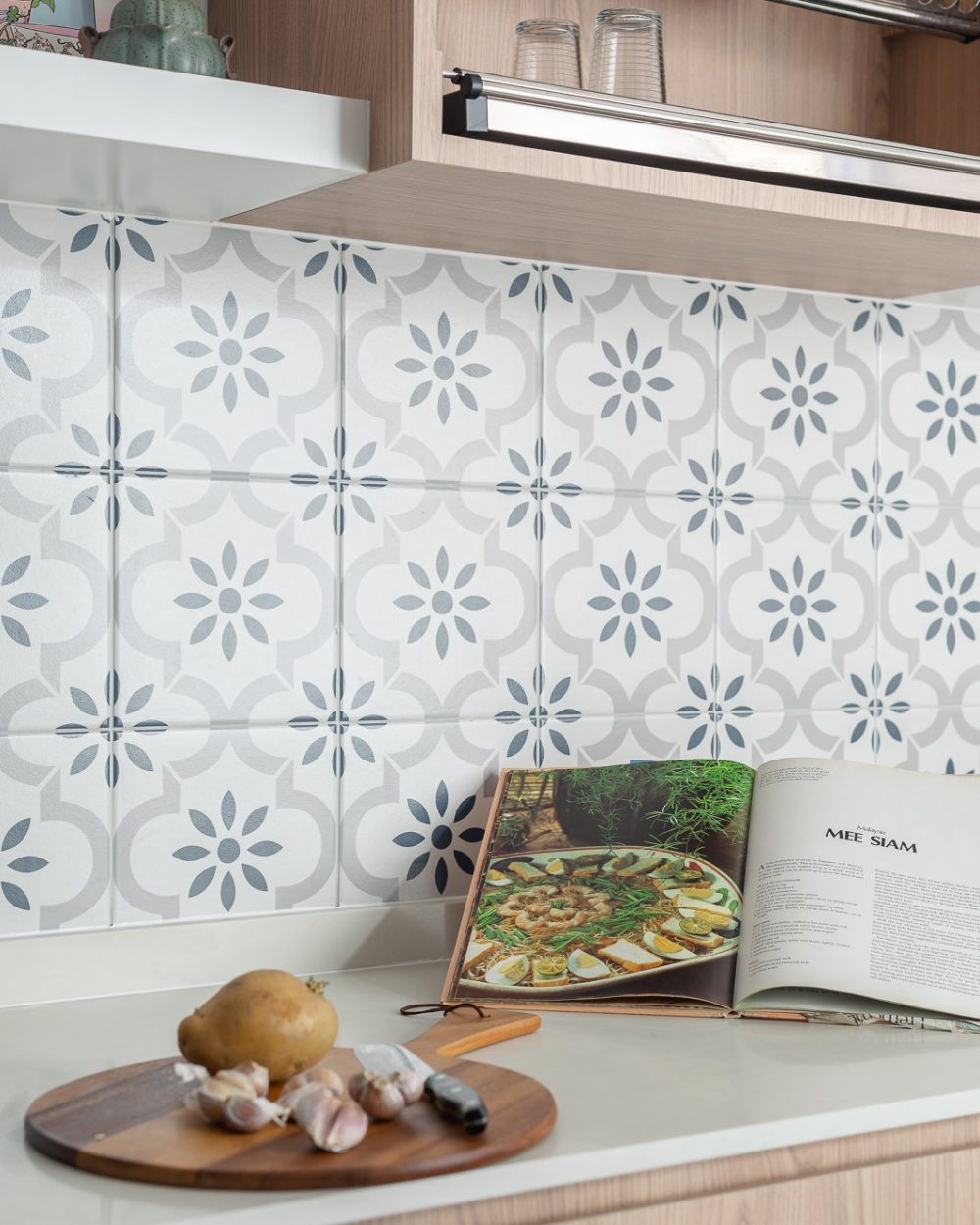 Close-up of grey and white Peranakan-style patterned tile backsplash with light oak cabinets and white quartz countertop