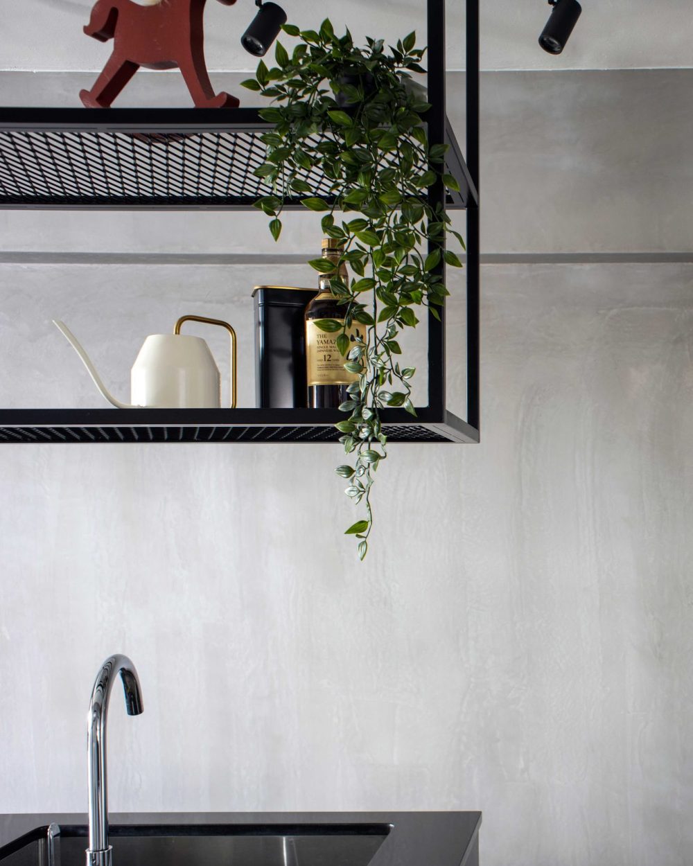 A hanging black shelving unit displays a vintage rocking horse, trailing greenery and a bottle of Yamazaki whisky.