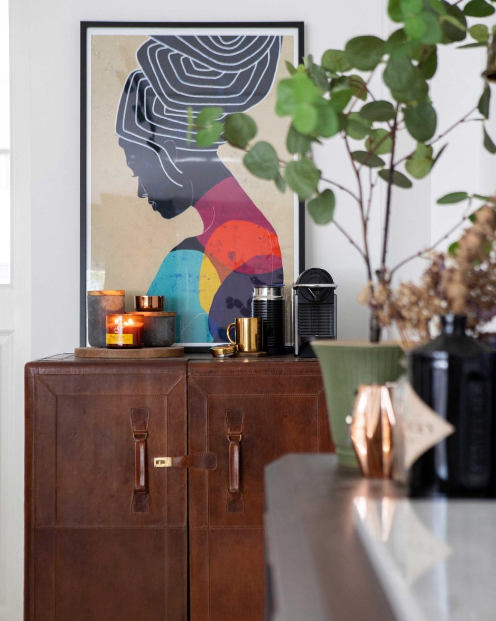 Framed art, candles and coffee essentials are styled on a leather trunk cabinet, adding warmth to the living area.
