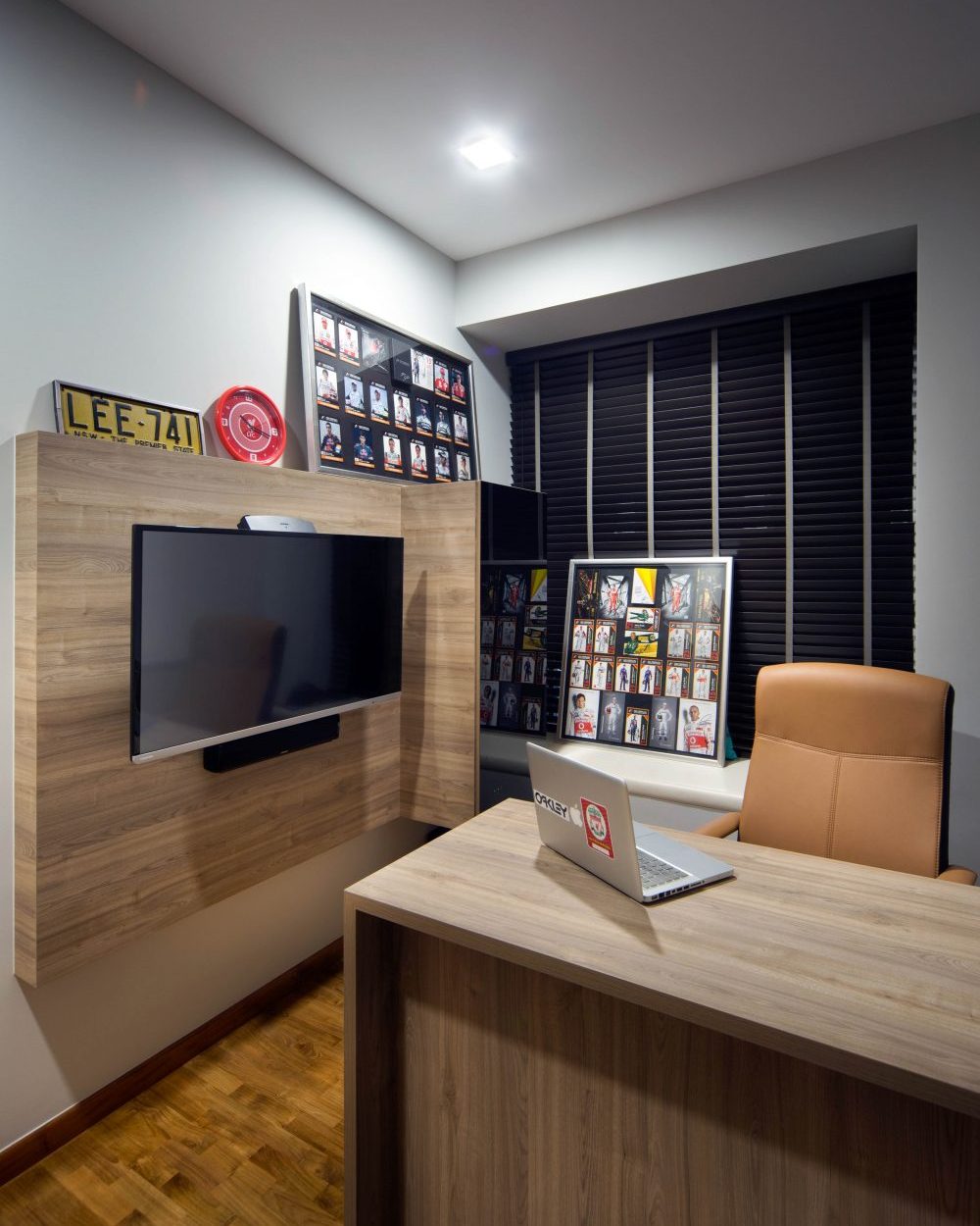 Framed memorabilia and a vintage number plate personalise this home office, built around a wall-mounted TV and timber desk.