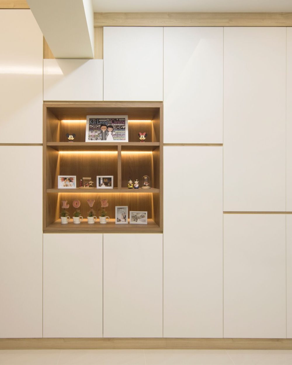 A backlit display niche within the storage wall holds wedding keepsakes and family photos, a personal touch within the otherwise clean-lined joinery.