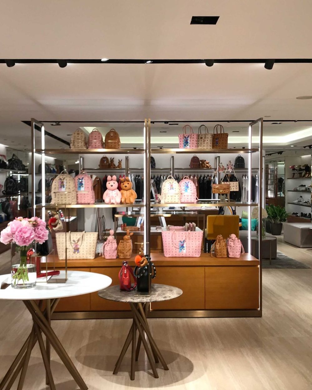 Backpacks, totes and bear and rabbit bag charms displayed on open shelving with fresh flowers.