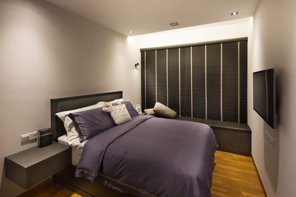 Deep purple bedding pairs with a dark upholstered headboard and a built-in window seat, wall-mounted TV included for evenings in.