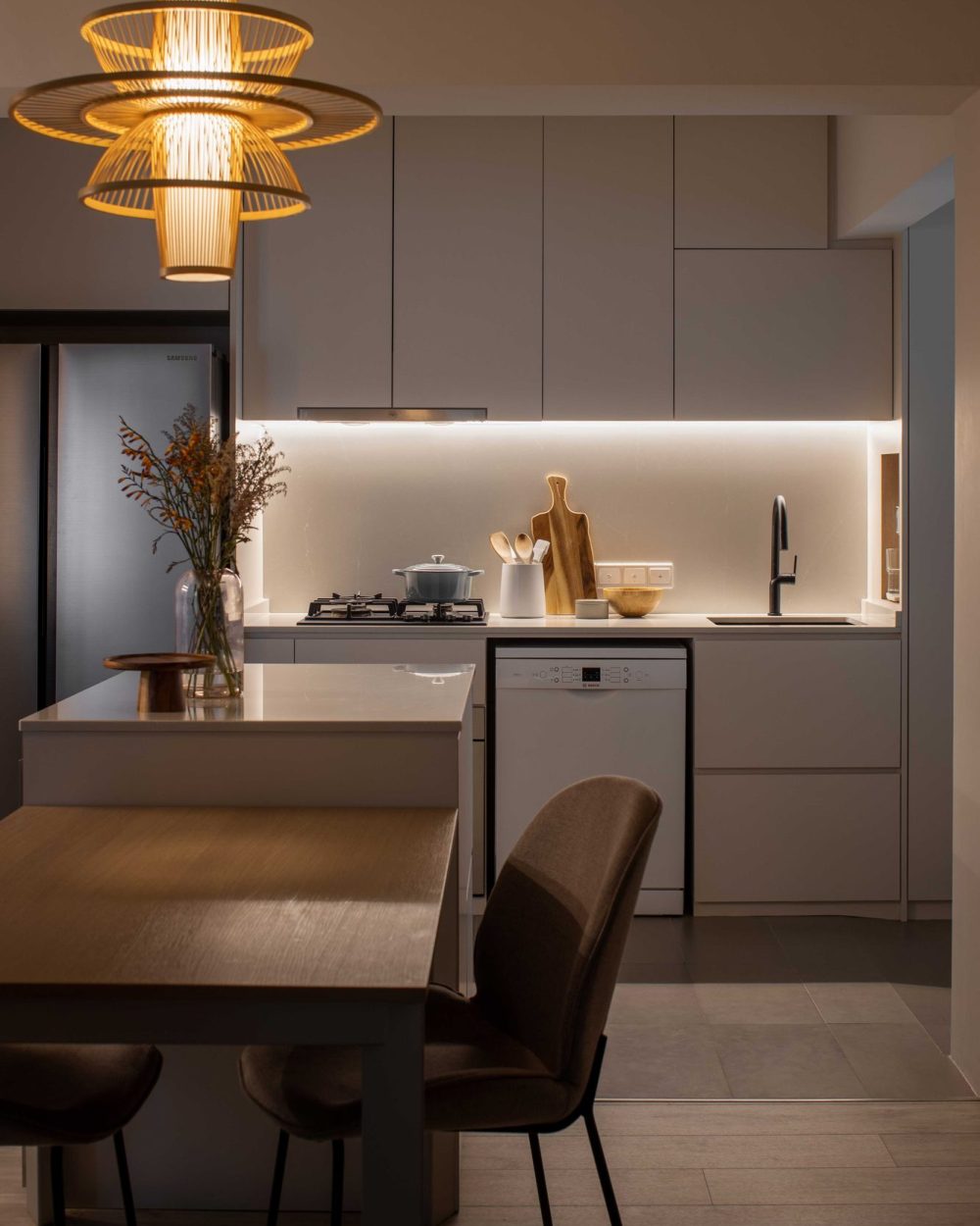 The same rattan pendant lighting extends into the kitchen, paired with soft grey cabinetry and a marble-look backsplash.