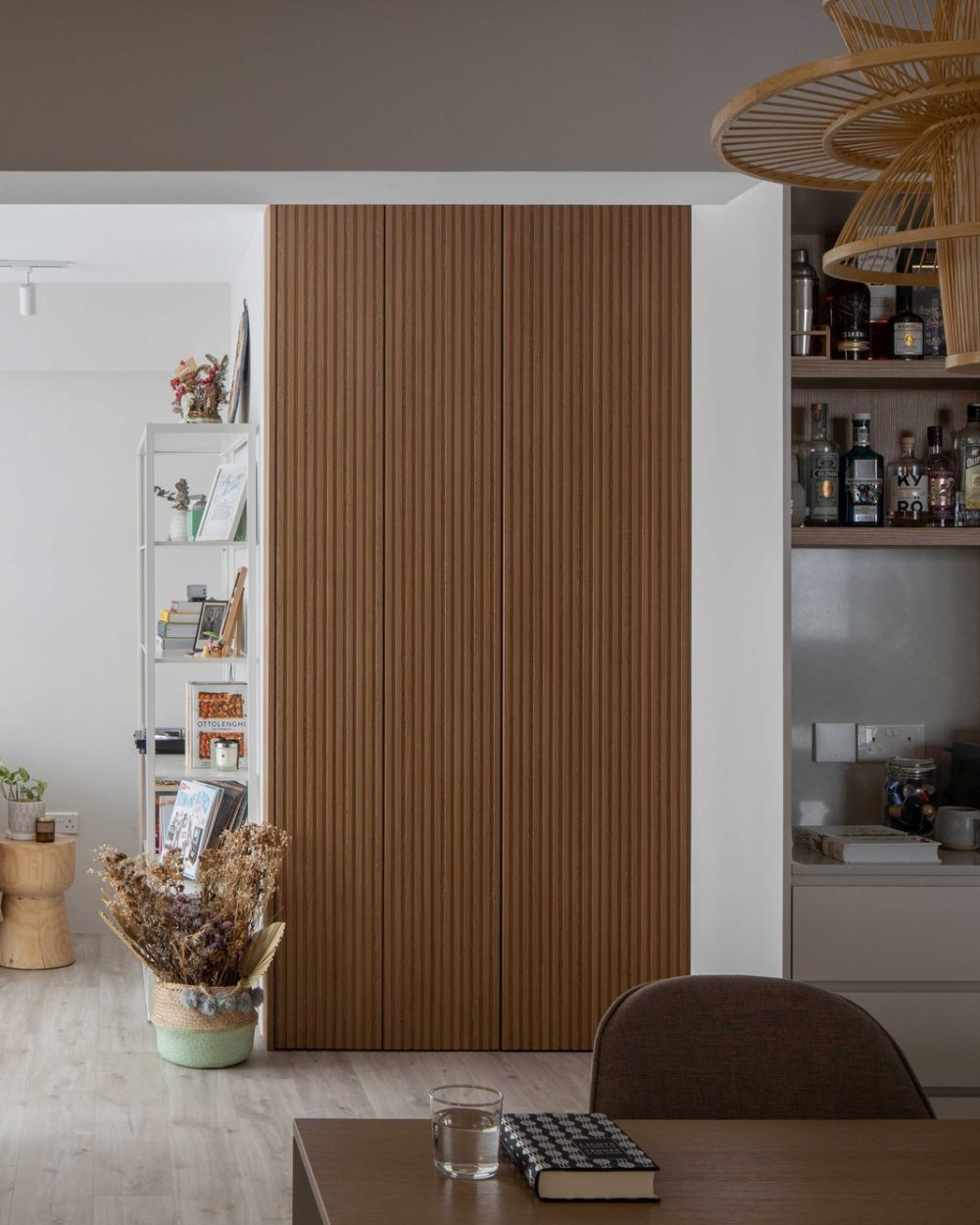 A tiered rattan pendant light hangs beside a reeded oak wardrobe door, with a built-in bar nook glimpsed through the opening.