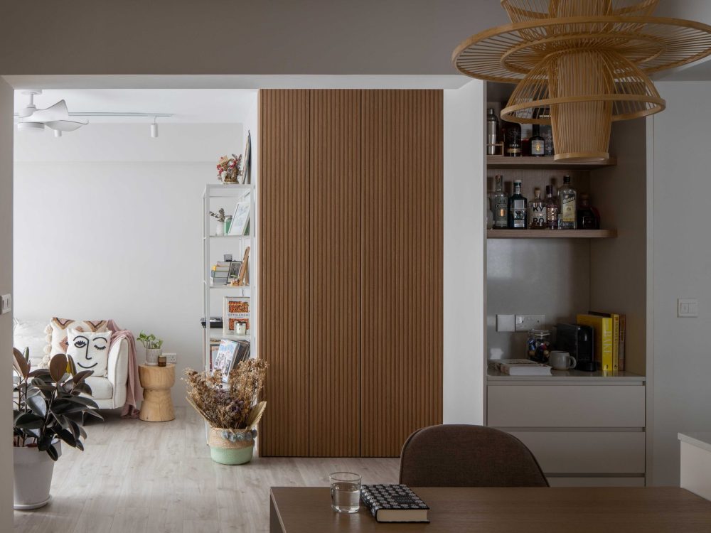A tiered rattan pendant light hangs beside a reeded oak wardrobe door, with a built-in bar nook glimpsed through the opening.